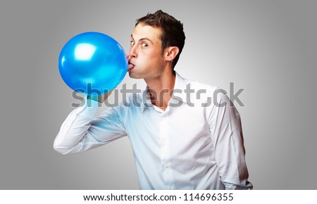 Portrait Of Young Man BlowingÃ?Â Balloon On Grey Background
