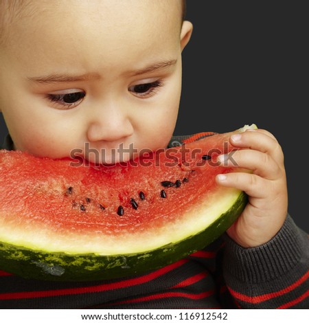 portrait of a handsome kid biting a watermelon over black background