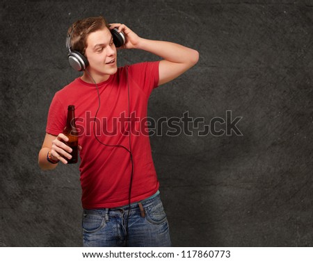 portrait of young man listening music and holding beer against a grunge wall