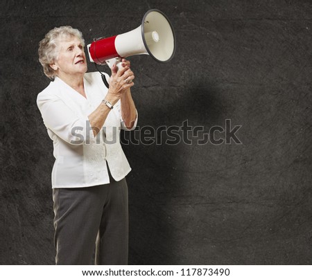 portrait of senior woman holding megaphone over grunge wall