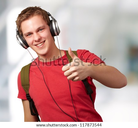 portrait of cheerful young student listening music and gesturing good with headphones indoor