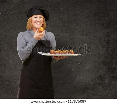 portrait of middle aged cook woman holding a homemade muffin against a grunge wall