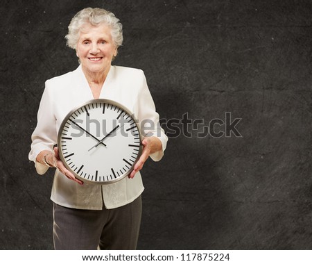 portrait of a happy senior woman holding clock against a grunge background