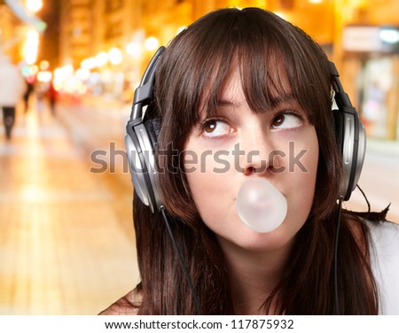 portrait of young woman listening to music with bubble gum at night city