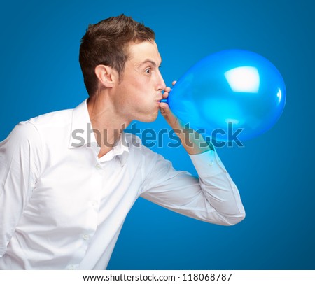 Portrait Of Young Man Blowing A Balloon Isolated On Blue Background