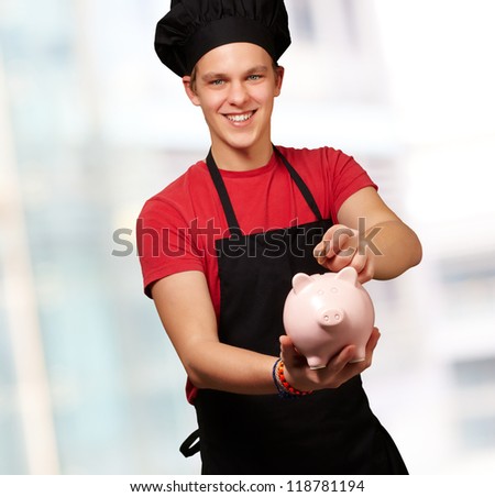 male chef holding a piggy bank and a coin, indoor
