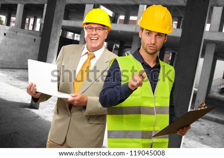 Portrait Of Two Architect Engineers Holding Laptop And Writing Pad, Indoors