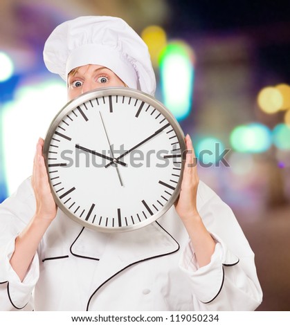 female chef hiding behind a clock at a street by night