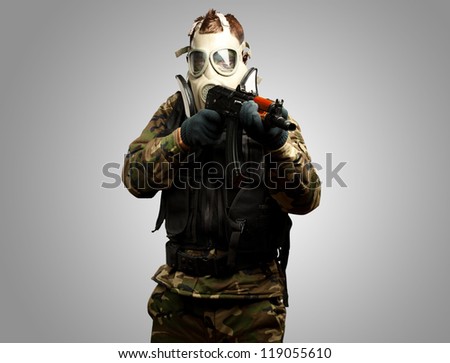 Portrait Of A Soldier With Gas Mask Aiming With Gun against a grey background