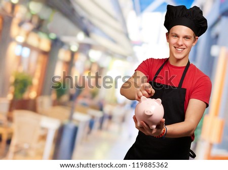 male chef holding a piggy bank and a coin, indoor