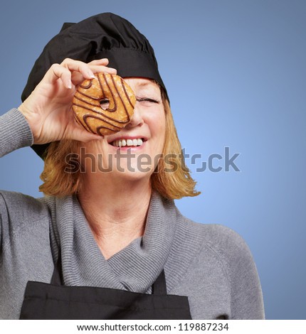 Middle aged cook woman looking through a donut over blue background