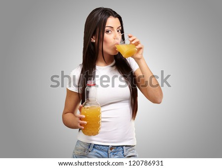 portrait of young girl drinking orange juice against a grey background