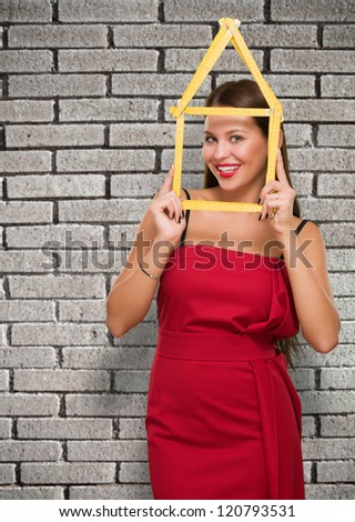 Happy Young Woman Looking Through House Frame against a brick wall