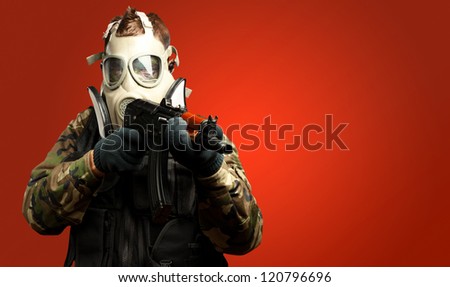 Portrait Of A Soldier With Gas Mask Aiming With Gun against a red background