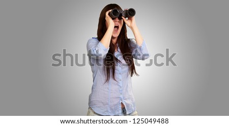 Portrait Of A Young Woman Looking Through Binoculars On Gray Background