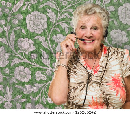 Portrait Of Cheerful Senior Woman With Telephone Headset Against Wallpaper