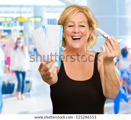 Woman Holding Boarding Pass And Miniature Airplane, Indoors