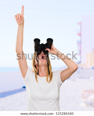 woman looking through binoculars and pointing up at the beach