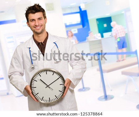 Happy Male Doctor Holding Clock, Indoors
