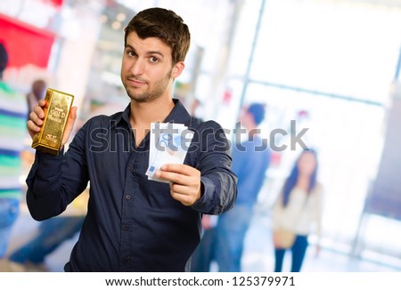 Young Man Holding Gold Bar And Euro Currency, Indoors