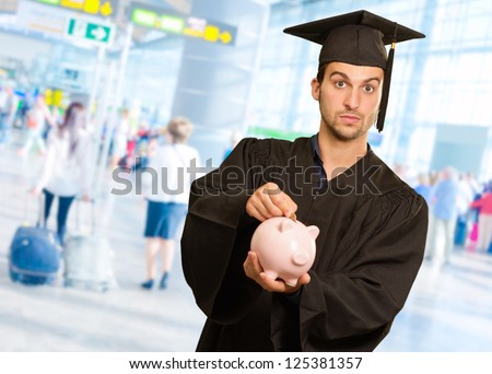 Graduate Man Inserting Coin In Piggy bank, Indoor