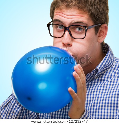 Young Man Blowing Blue Balloon against a blue background