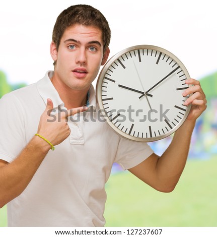 Portrait Of A Young Man Pointing at a Wall Clock at a park