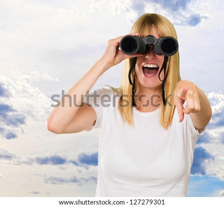 woman looking through binoculars and pointing against a cloudy sky background