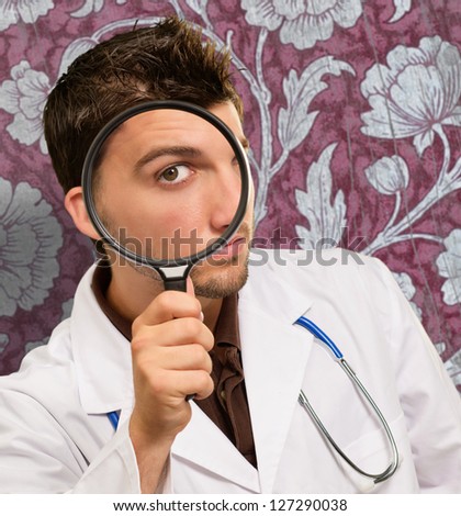Portrait Of A Doctor Looking Through Magnifying Glass Against Wallpaper