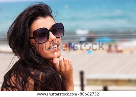 young pretty girl wearing sunglasses smiling with the beach as a background