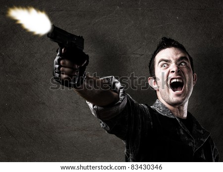 man shooting a gun against a eroded wall