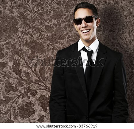 portrait of young man wearing suit and sunglasses against a vintage wall