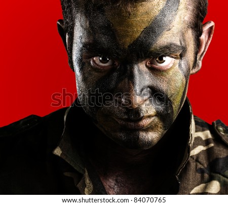 young soldier face with jungle camouflage paint on red background