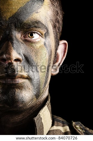 portrait of young soldier face with jungle camouflage paint against a black background