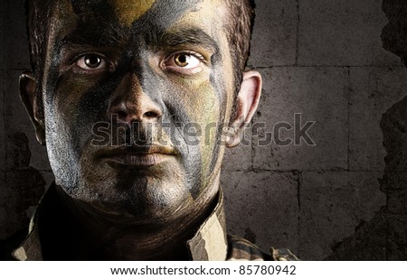 portrait of young soldier face painted with jungle camouflage against a grunge bricks wall