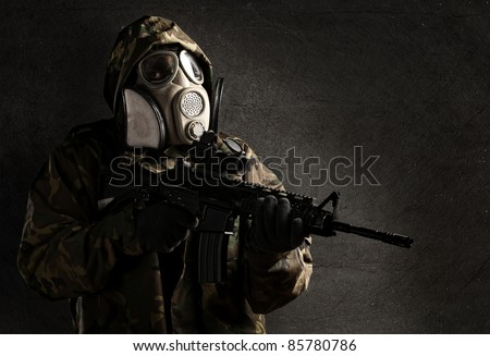 armed soldier with gas mask wearing a camouflage uniform against a wall