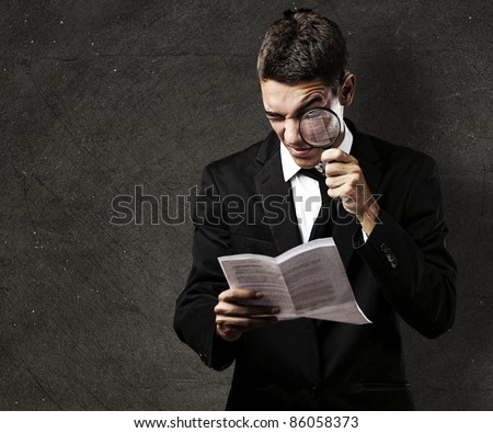 portrait of handsome young man reading a contract through a magnifying glass against a grunge background