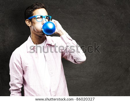 portrait of young man inflating a balloon against a grunge wall