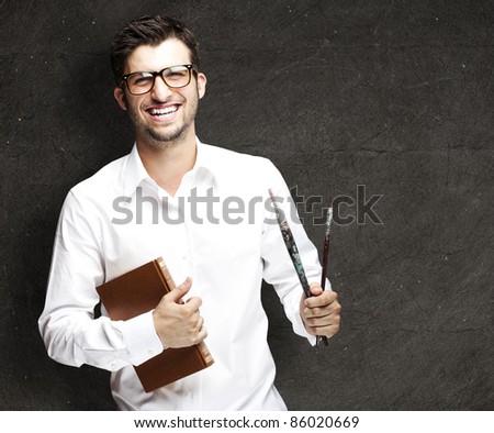 portrait of a handsome young student holding paintbrushes against a vintage wall - stock photo