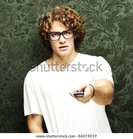 portrait of young man with glasses changing channel with tv control
