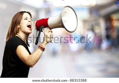 portrait of young woman shouting using megaphone against a crowded place