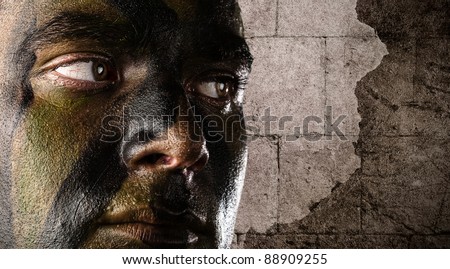portrait of young soldier face painted with jungle camouflage against a grunge bricks wall