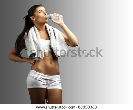 portrait of young woman wearing sport clothes and drinking water against a grey background - stock photo