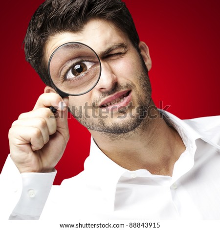 portrait of young man looking through a magnifying glass over red background