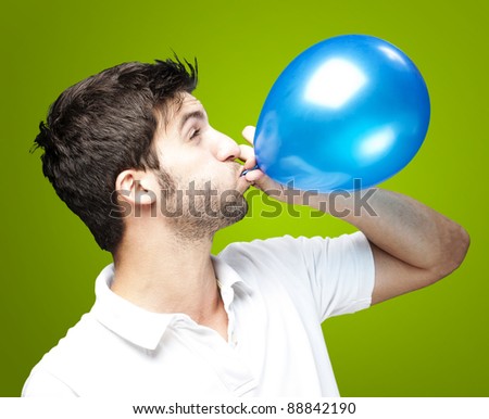 portrait of young man blowing a balloon over green background