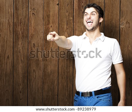 portrait of young man pointing with finger against a wooden wall