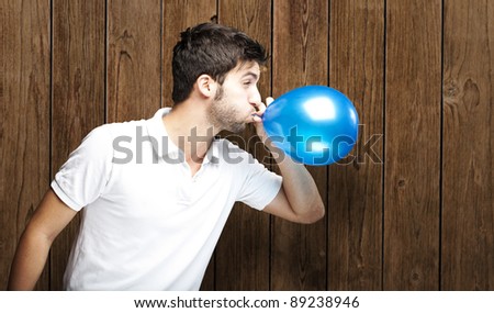 portrait of young man blowing balloon against a wooden wall