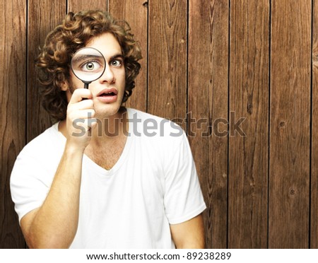 surprised man looking through a magnifying glass against a wooden wall