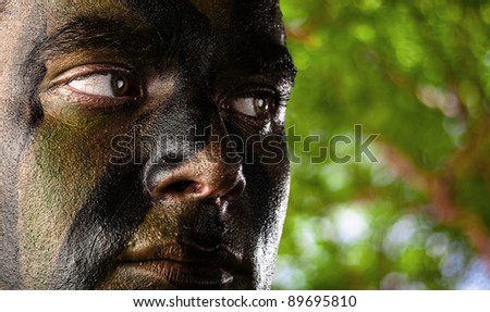 portrait of young soldier face painted with jungle camouflage in the jungle