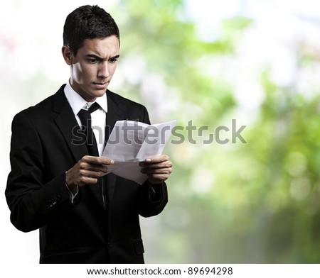 portrait of young business man reading a contract against a park background
